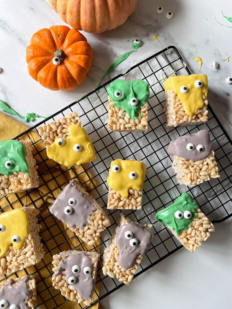 MM Rice Krispie Treats - The Delicious Monster Mash Treats 6 MM rice krispie treats on a cooling rack with pumpkins scattered around