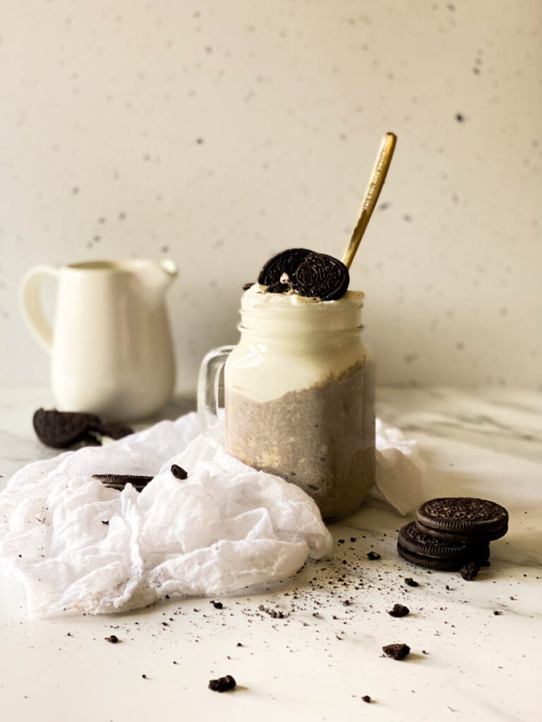 Tastiest Oreo Overnight Oats, Quick Breakfast Recipe 5 oreo overnight oats in a jar with a spoon, oreo cookies, milk jug and towel on sides