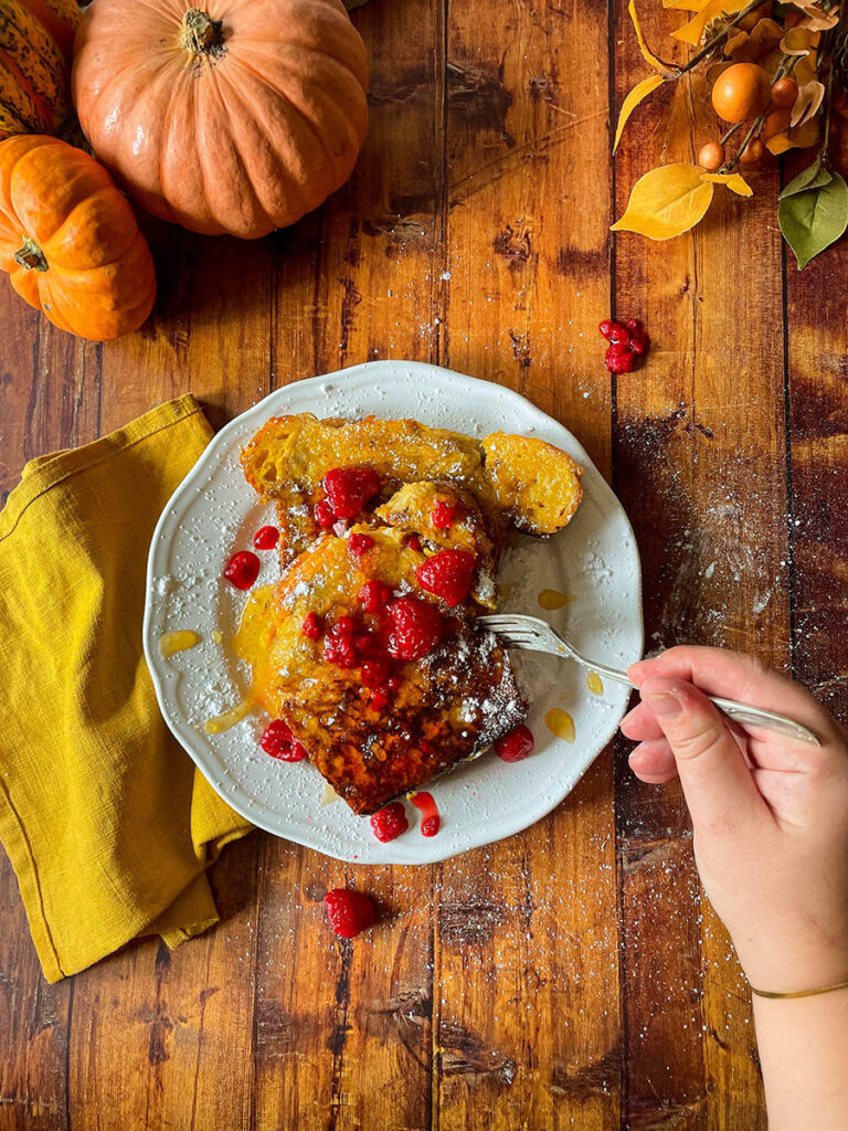 Delicious Pumpkin Brioche French Toast Recipe 10 pumpkin brioche french toast with honey and raspberries on a white plate with icing sugar, pumpkins and foliage on the background