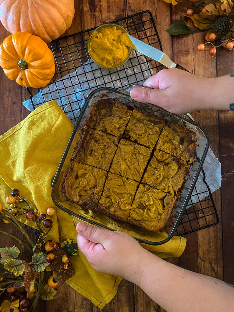 Irresistible Vegan Pumpkin Brownies: A Spooktacular Treat 1 vegan pumpkin brownie in a glass tray over a cooling rack with a yellow napkin and some pumpkins scattered around