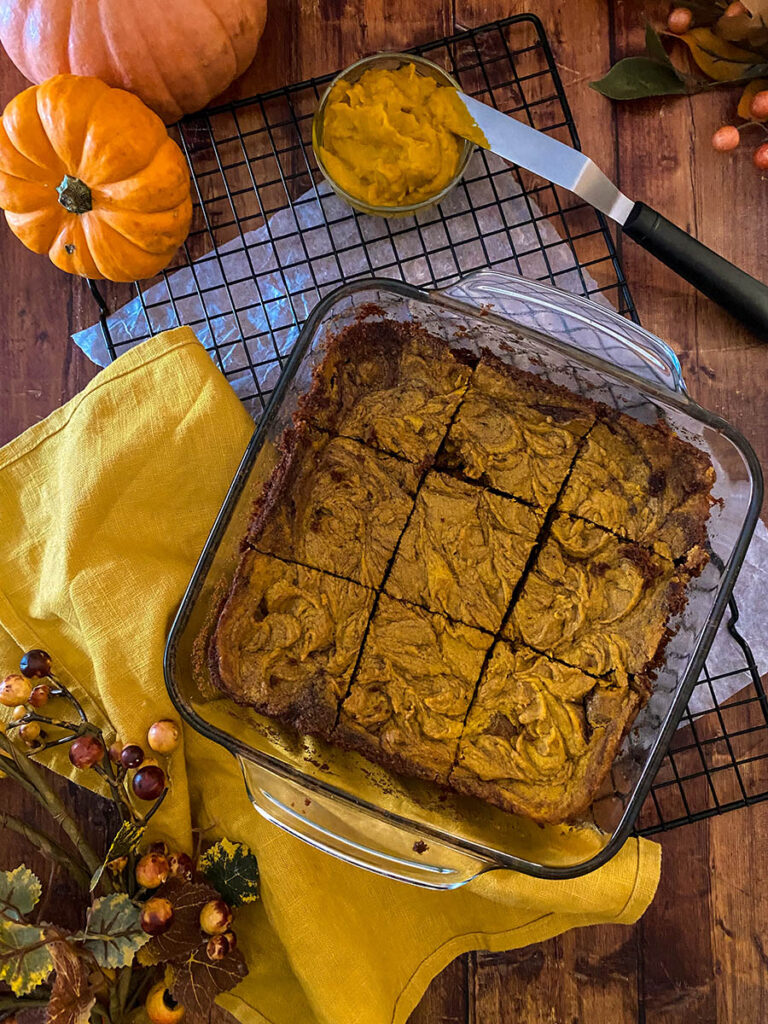 Irresistible Vegan Pumpkin Brownies: A Spooktacular Treat 2 vegan pumpkin brownie in a glass tray over a cooling rack with a yellow napkin and some pumpkins scattered around