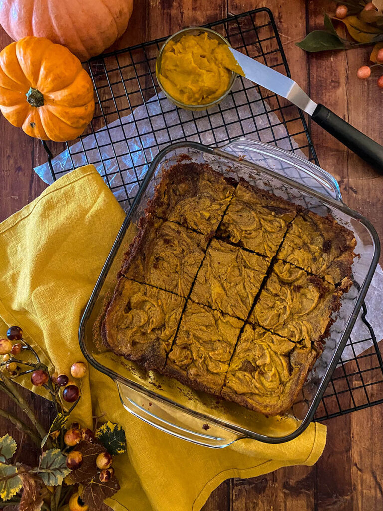 Irresistible Vegan Pumpkin Brownies: A Spooktacular Treat 6 vegan pumpkin brownie in a glass tray over a cooling rack with a yellow napkin and some pumpkins scattered around