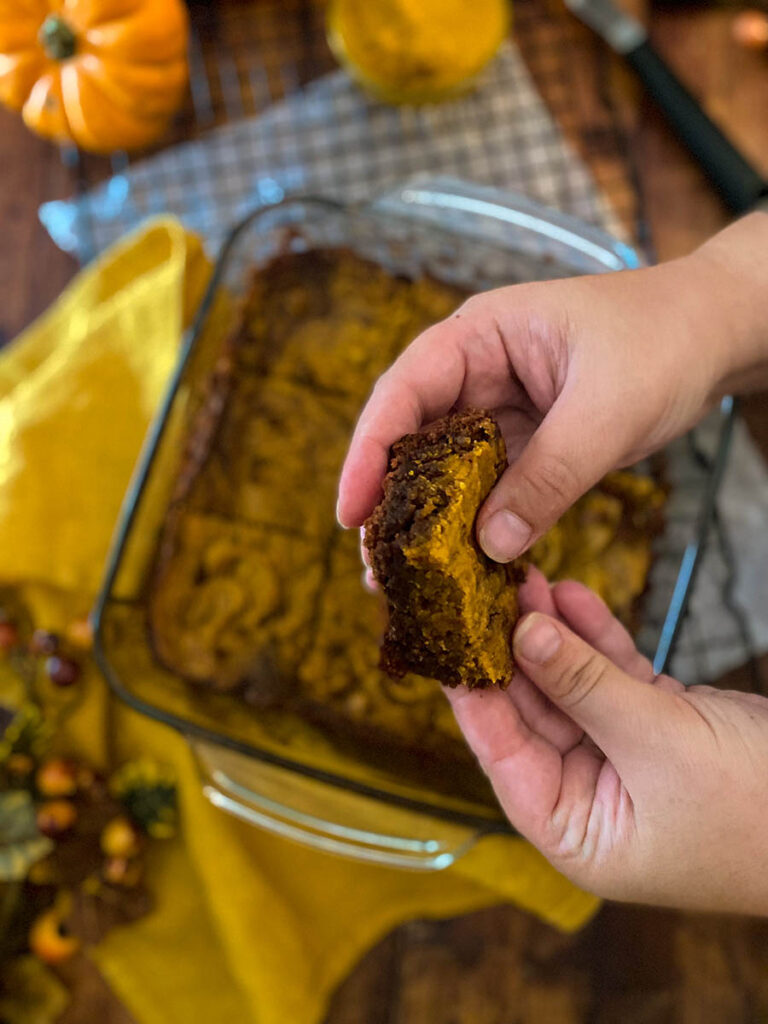 Irresistible Vegan Pumpkin Brownies: A Spooktacular Treat 7 vegan pumpkin brownie in a glass tray over a cooling rack with a yellow napkin and some pumpkins scattered around