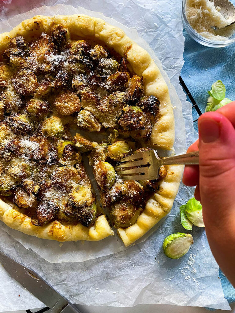 brussel sprout galette on a cooling rack over a light blue napkin, with cheese in a small bowl and red ribbon on the background