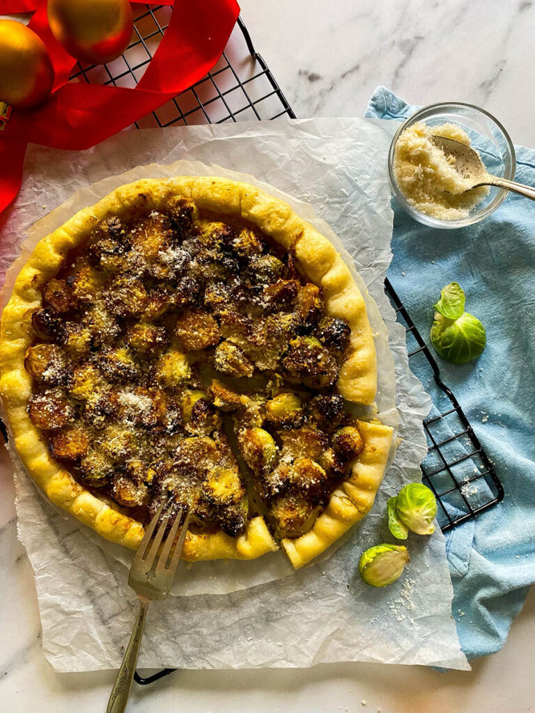 brussel sprout galette on a cooling rack over a light blue napkin, with cheese in a small bowl and red ribbon on the background