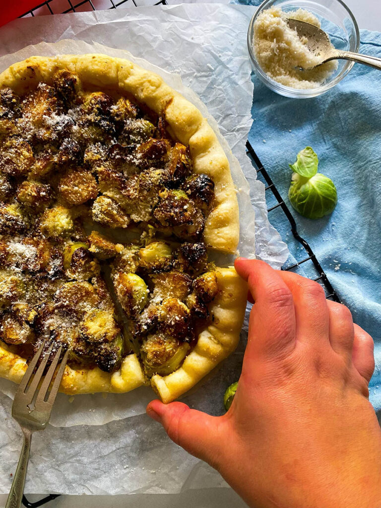 brussel sprout galette on a cooling rack over a light blue napkin, with cheese in a small bowl and red ribbon on the background