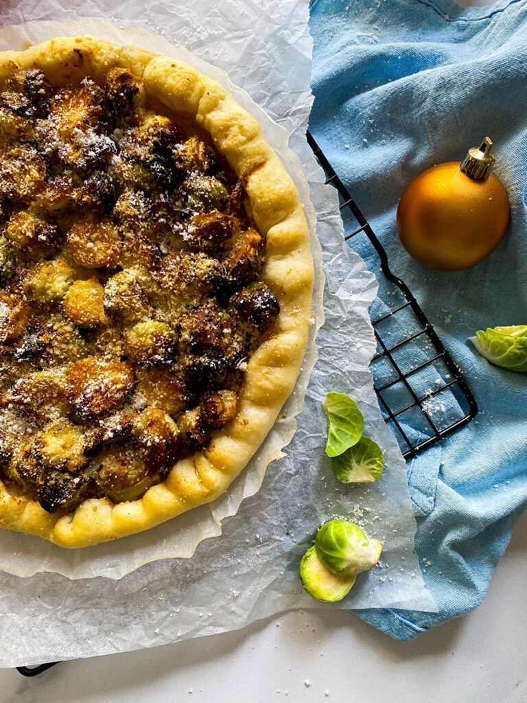 brussel sprout galette on a cooling rack over a light blue napkin, with cheese in a small bowl and red ribbon on the background