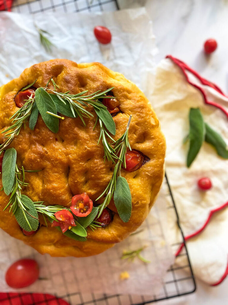 Christmas Focaccia: The Most Delicious Bread With A Festive Twist 5 Christmas focaccia on a cooling rack with tomatoes, rosemary and sage, over a red and white napkin