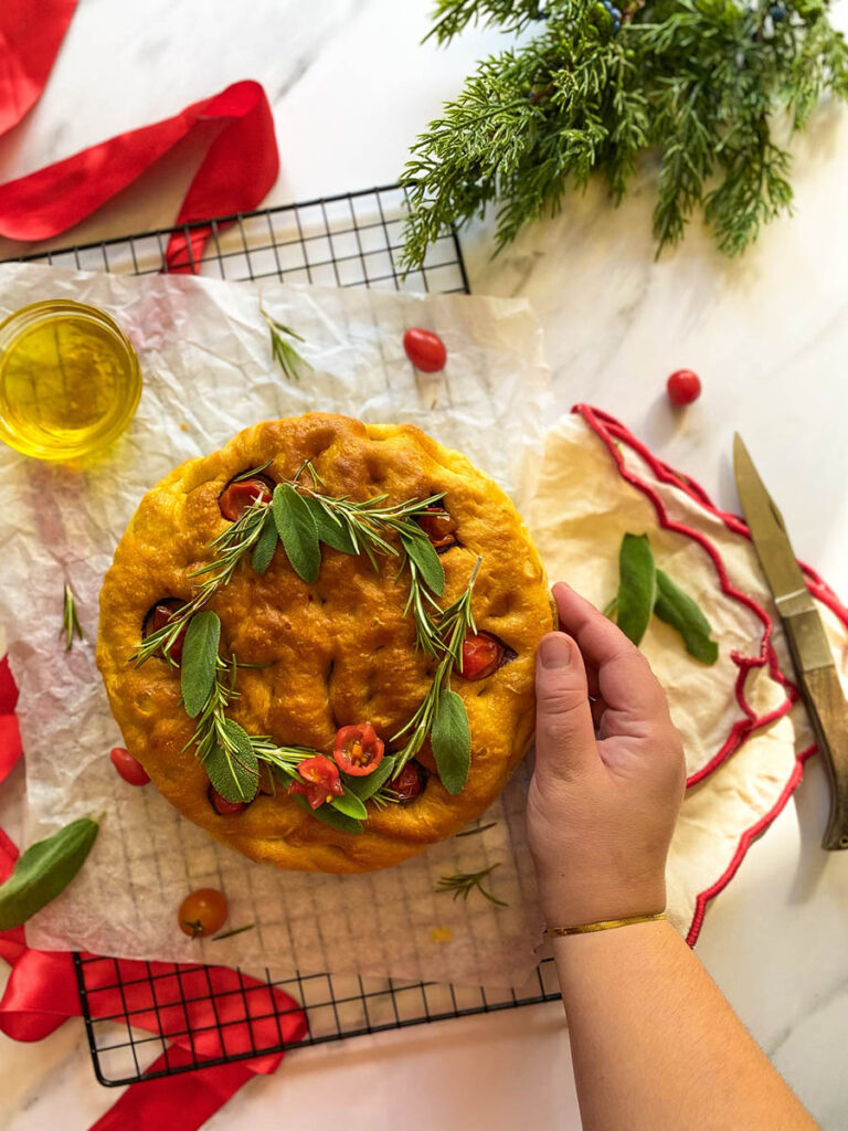 Christmas Focaccia: The Most Delicious Bread With A Festive Twist 6 Christmas focaccia on a cooling rack with tomatoes, rosemary and sage, over a red and white napkin