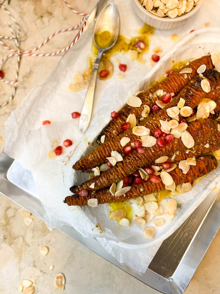 hassleback carrots on a silver tray with shaved almonds and pomegranate seeds over a marble top 