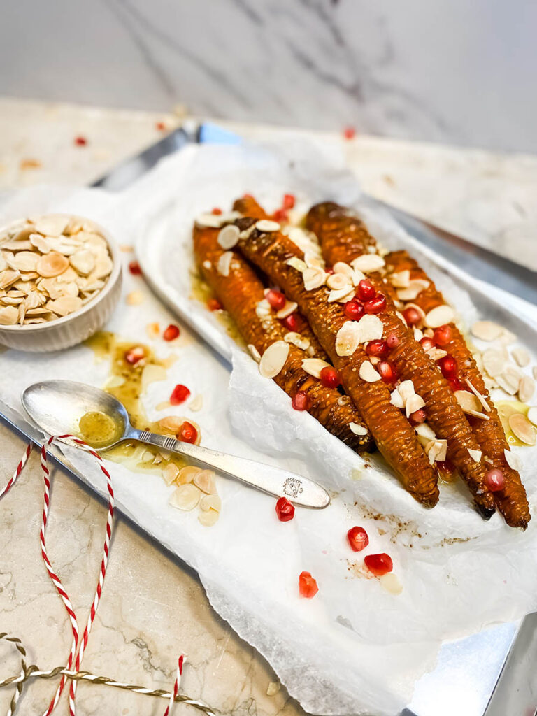 hassleback carrots on a silver tray with shaved almonds and pomegranate seeds over a marble top 