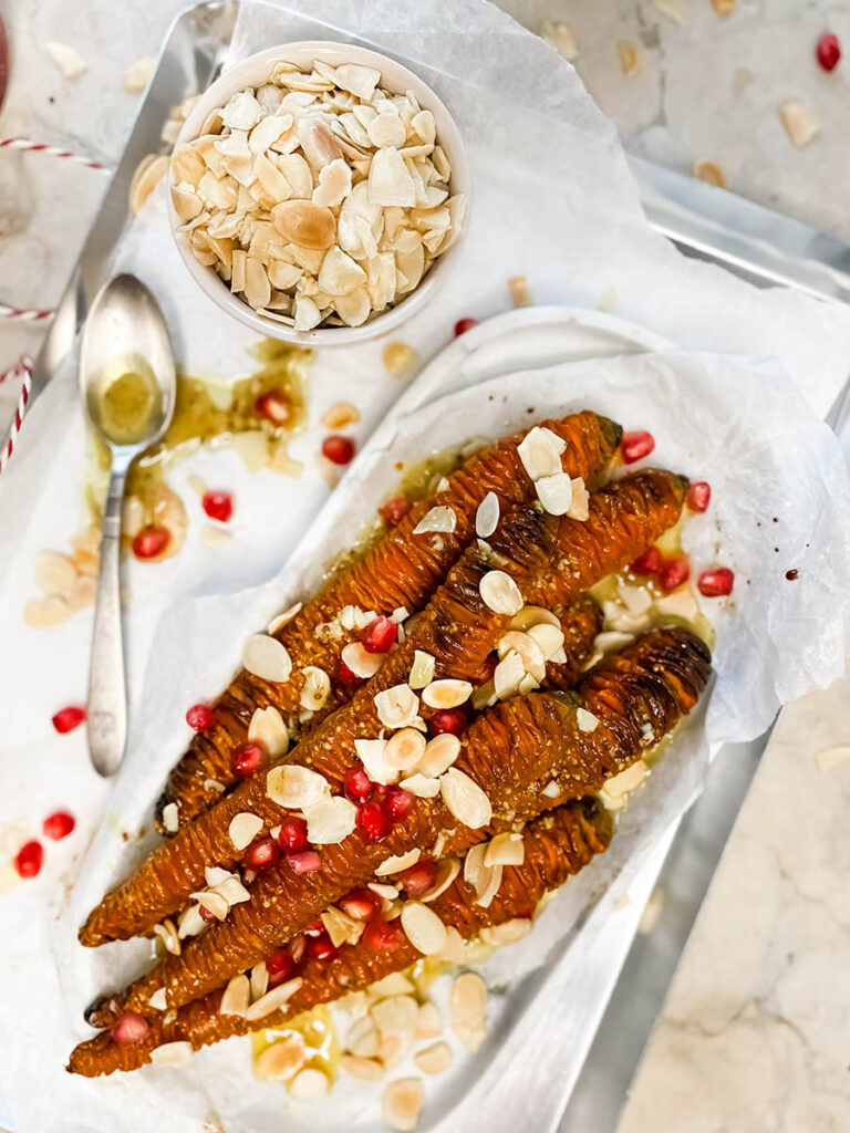 hassleback carrots on a silver tray with shaved almonds and pomegranate seeds over a marble top 