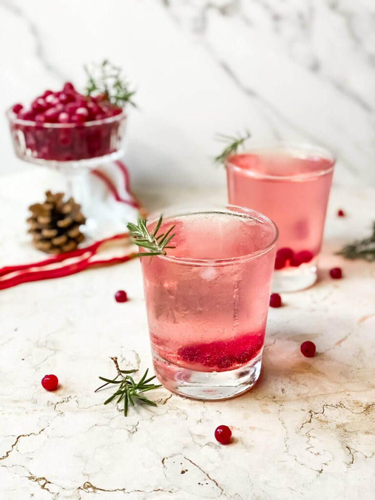 Super Mistletoe Kiss Cocktail Recipe for a Jolly Holiday Season 2 mistletoe kiss cocktail glasses with fresh rosemary and a red ribbon on the background