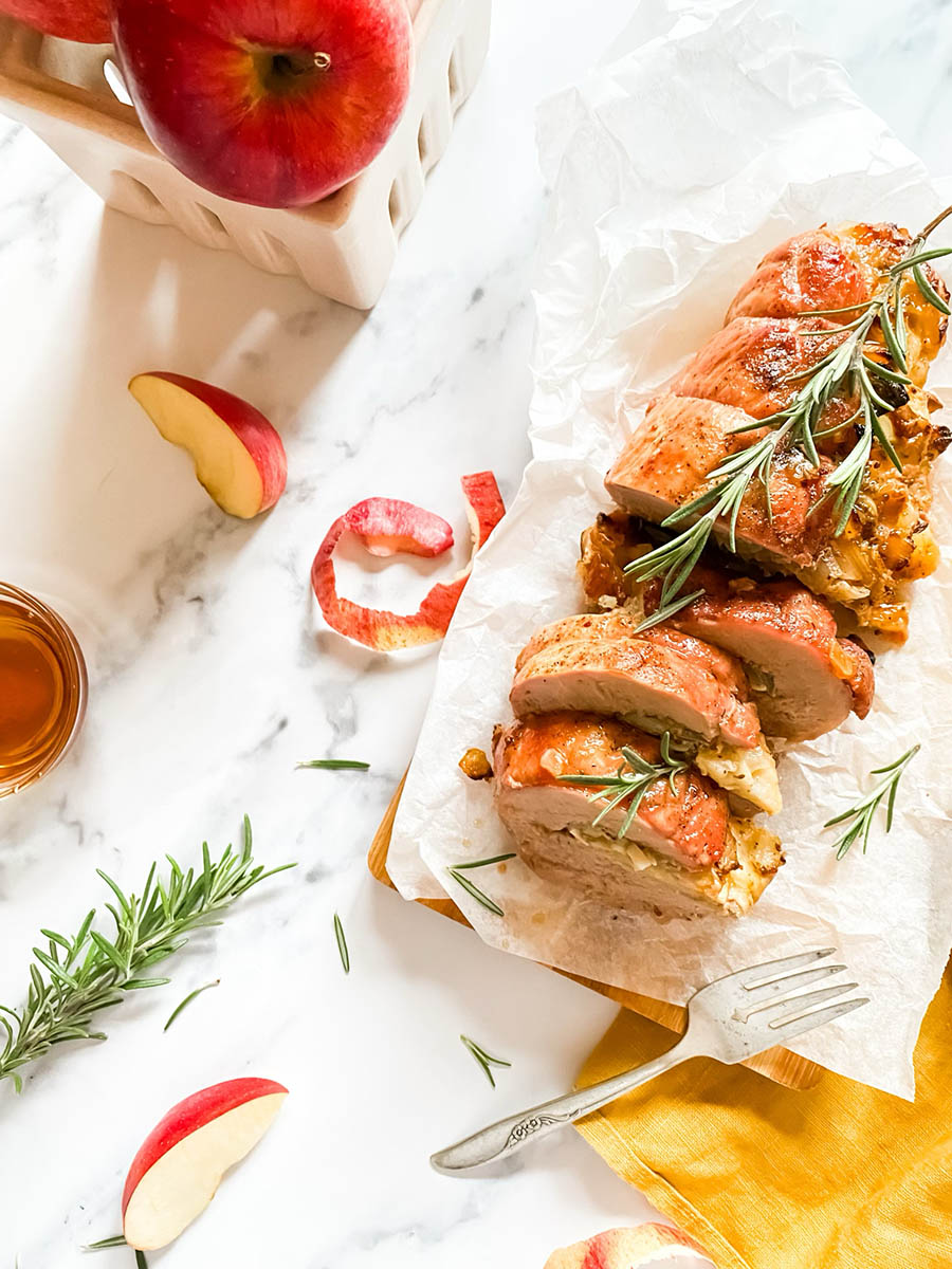 brie stuffed pork tenderloin fillet over parchment paper with apples and a fork over a wooden board