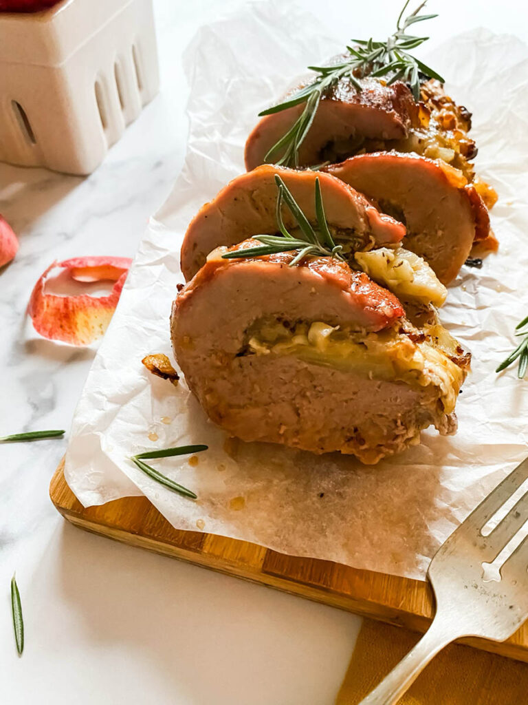 detail of brie stuffed pork tenderloin fillet over parchment paper with apples and a fork over a wooden board