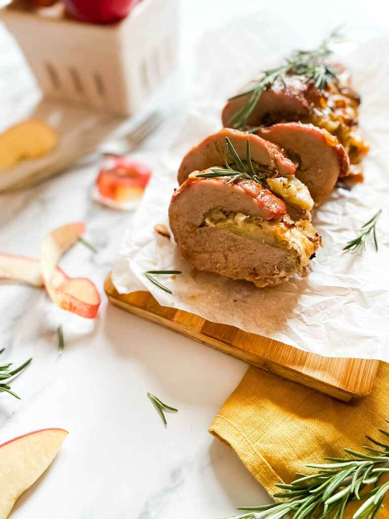 detail of brie stuffed pork tenderloin fillet over parchment paper with apples and a fork over a wooden board