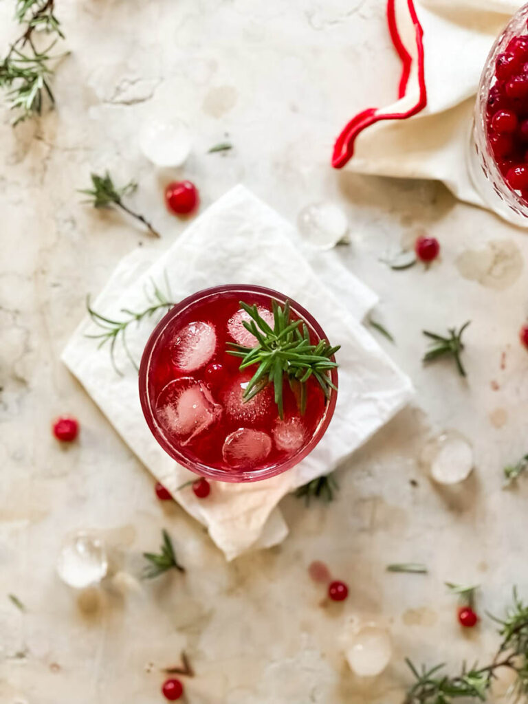 Sip into the Season: Delicious Maple Cranberry Bourbon Cocktail Bliss 4 maple cranberry bourbon cocktail over some parchment paper with rosemary, cranberries and ice scattered around