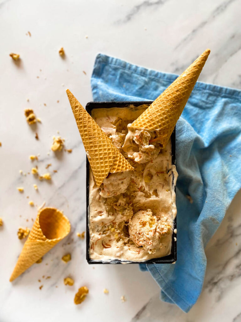 Easter Ice Cream Recipe No Churn 3 tin loaf with easter ice cream carrot cake flavoured, two cones on it, blue towel under, a cone on the side