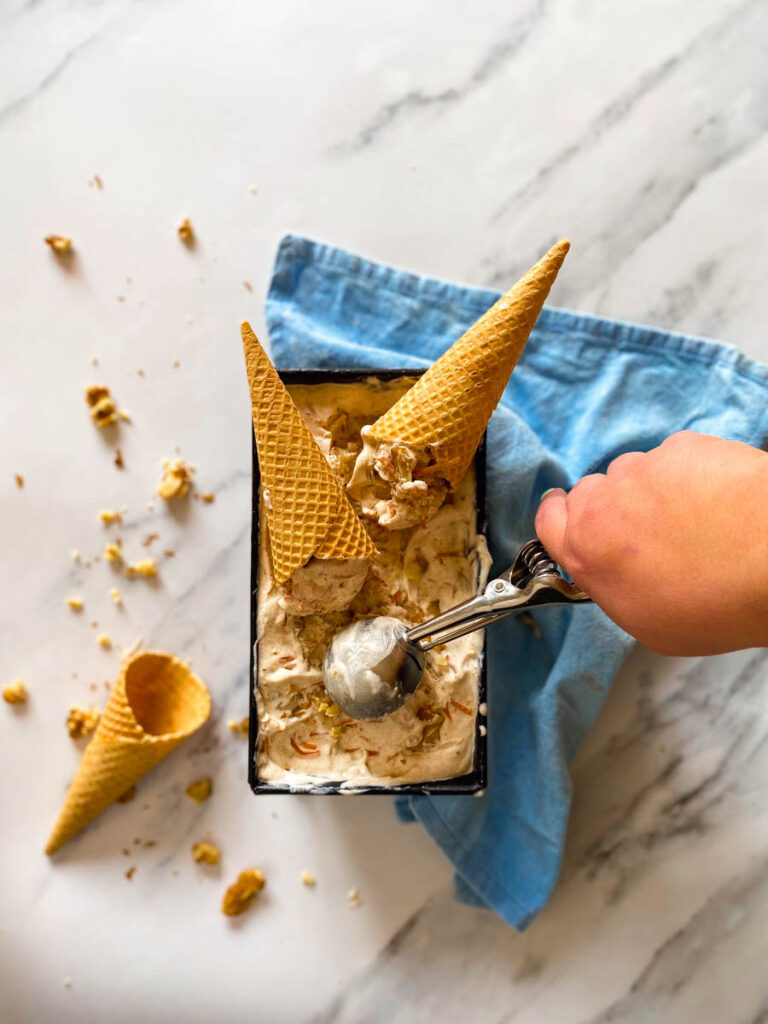 Easter Ice Cream Recipe No Churn 4 Hand scooping some easter ice cream carrot cake flavoured, two cones on it, blue towel under
