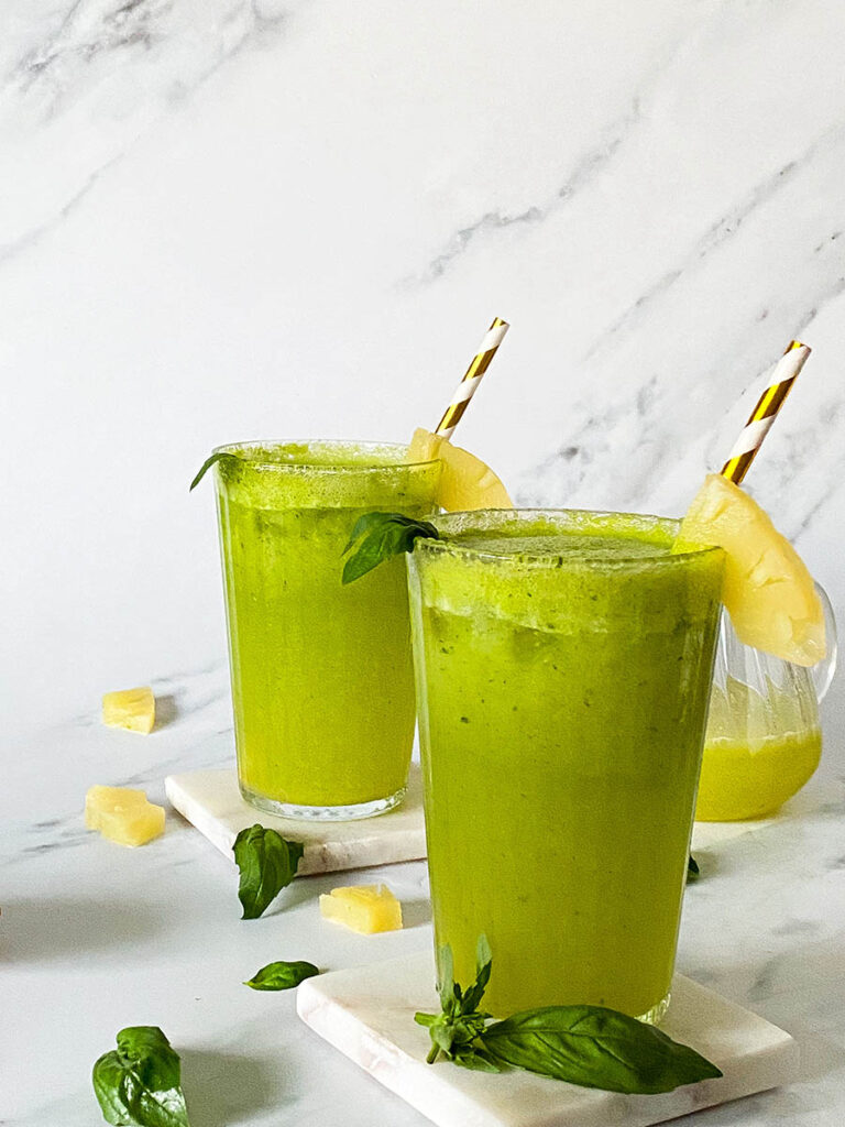pineapple basil mocktails over a marble background with scattered fresh basil leaves and pineapple chunks