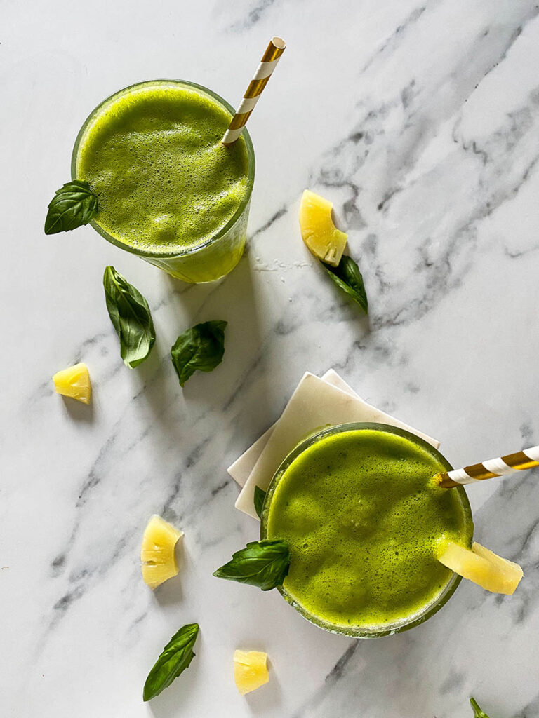 pineapple basil mocktails over a marble background with scattered fresh basil leaves and pineapple chunks