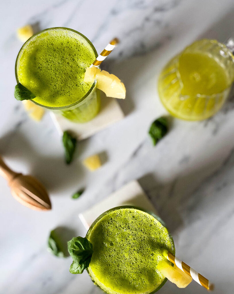 pineapple basil mocktails over a marble background with scattered fresh basil leaves and pineapple chunks