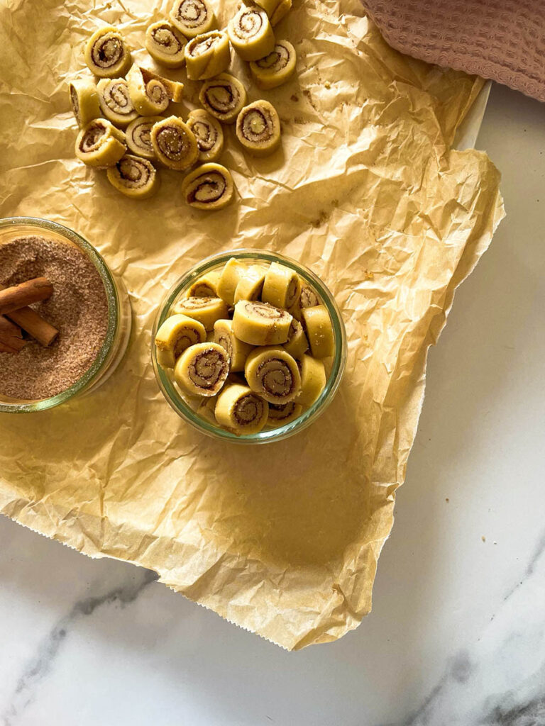 Cinnamon Bun Cookie Dough Bites: Delicious No Bake Snack 2 cinnamon bun cookie dough bites in a glass bowl with cinnamon and brown sugar next to it plus extra mini bites scattered around