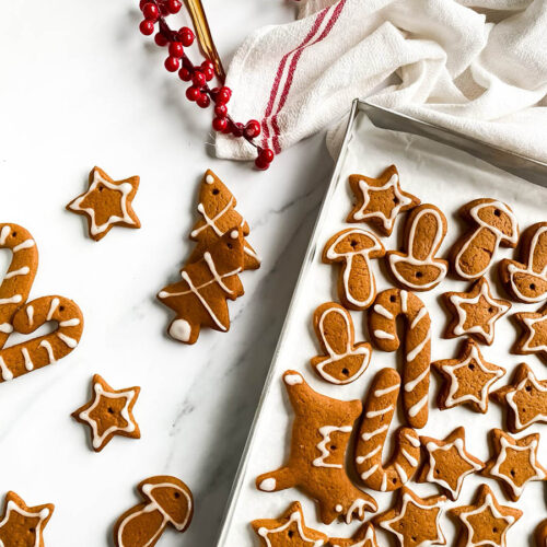 Adorable Christmas Gingerbread Ornaments, Easy & Quick 5 gingerbread ornaments on a silver tray more ornaments scattered around, a white and red towel behind and some decor, on a marble background