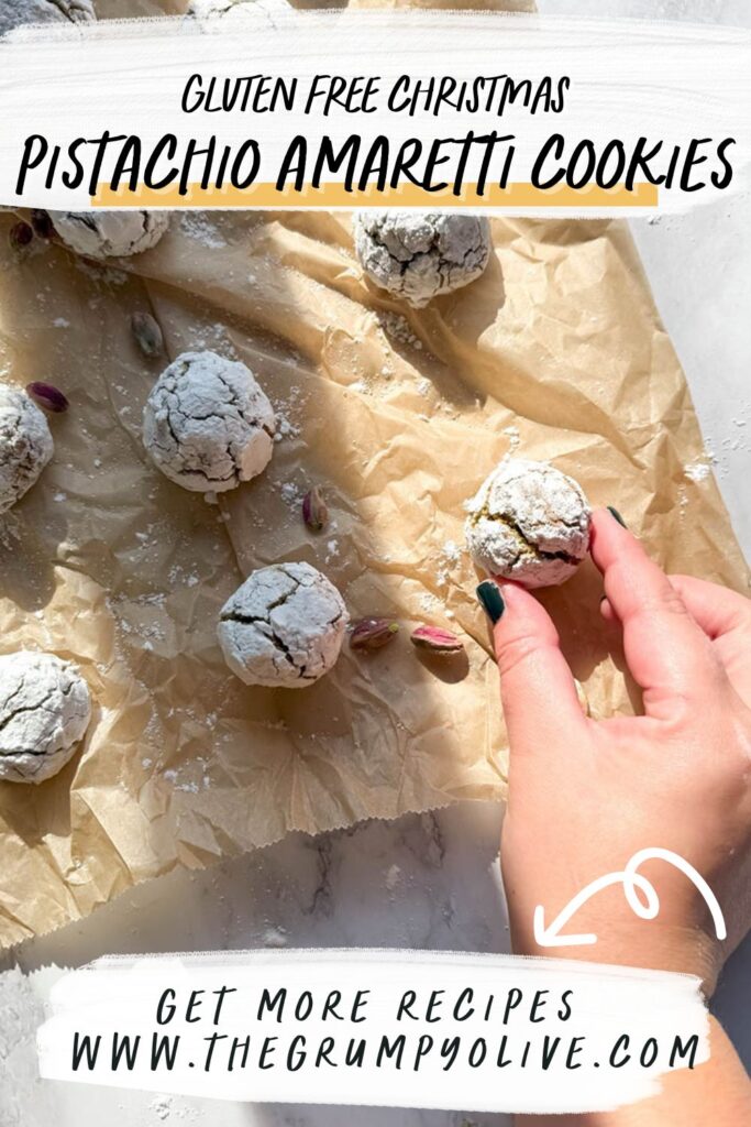 Yummy Pistachio Amaretti Cookies, For The Most Perfect Christmas 11 A banner image with text overlay that reads "Gluten Free Christmas Pistachio Amaretti Cookies" at the top, and "Get More Recipes www.thegrumpyolive.com" at the bottom. A hand is holding a cookie on parchment paper, with scattered pistachios for decoration.