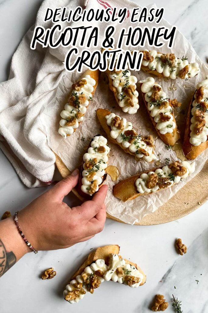 A styled image of crostini with the text overlay “Deliciously Easy Ricotta & Honey Crostini.” Each crostini is topped with piped ricotta, walnuts, honey, and thyme, surrounded by a cozy kitchen setting.