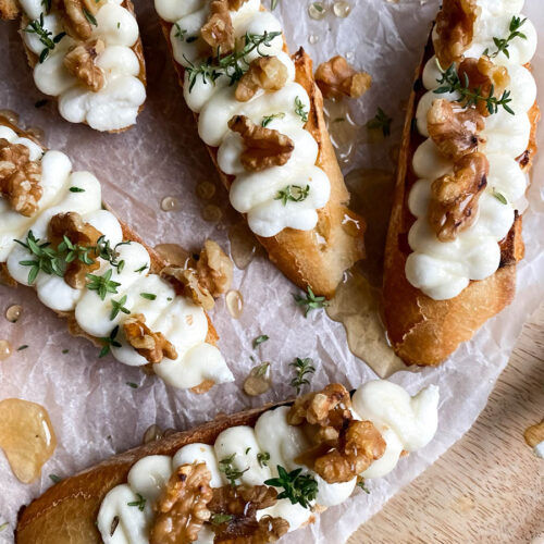 close up of whipped ricotta honey crostini on parchment paper and on a wooden board