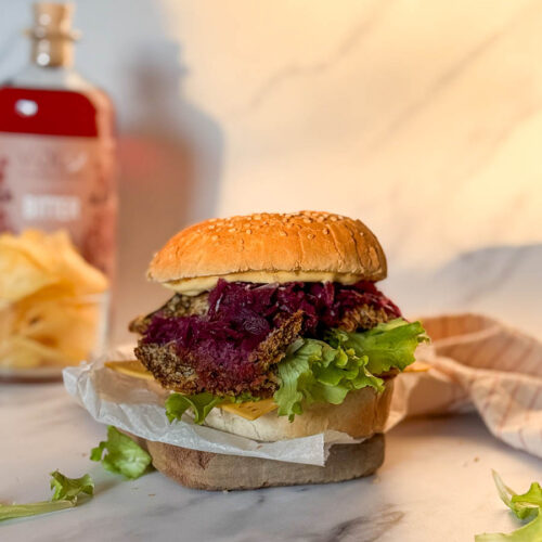 Asian-Inspired Oyster Mushroom Burgers, Easy & Vegan Recipe 4 oyster mushroom burger on a wood board, salad aroun, in the background a striped towel, crisps and a bottle of bitter, on a marble background