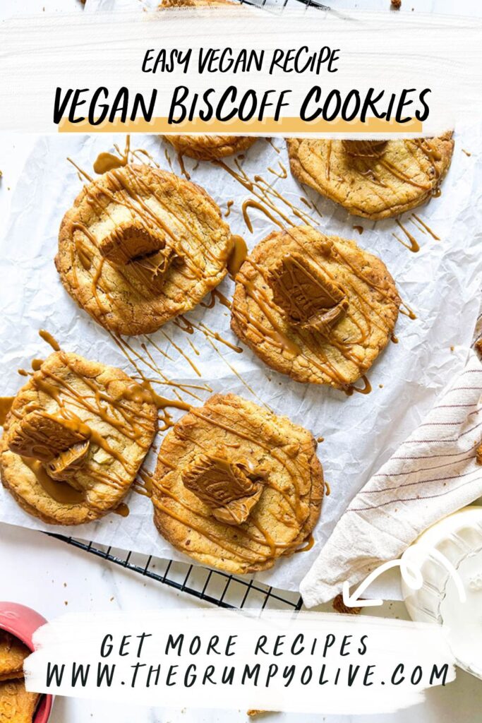 Vegan Biscoff Cookies, The Ultimate Recipe For Delicious Cookies 11 A batch of vegan Biscoff cookies on a black cooling rack, drizzled with caramel-like Biscoff spread and topped with small Biscoff biscuit pieces, placed on a sheet of white parchment paper. Crumbs are scattered on the marble surface, with a cup of milk and a pink mug filled with extra Biscoff biscuits nearby.