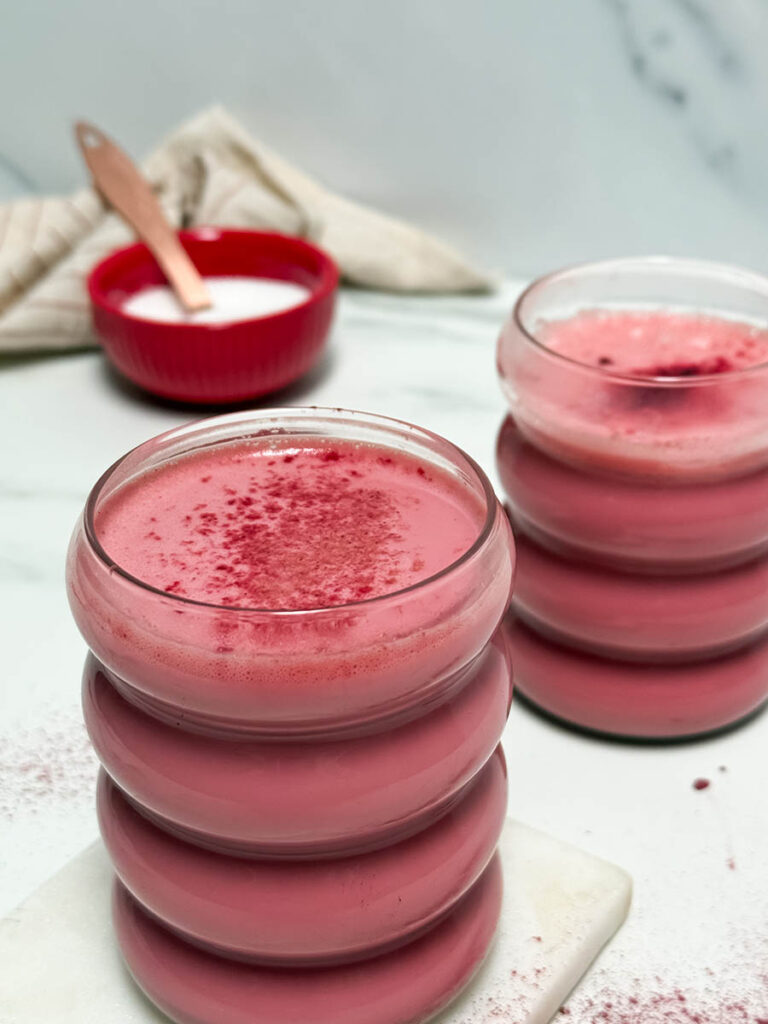 Red Latte Recipe, One Perfect For Valentine's Or Any Other Day Really 8 Two ribbed glasses of red latte with smooth foam and a sprinkle of red powder on top. The scattered powder on the white surface adds a playful, artisanal touch.