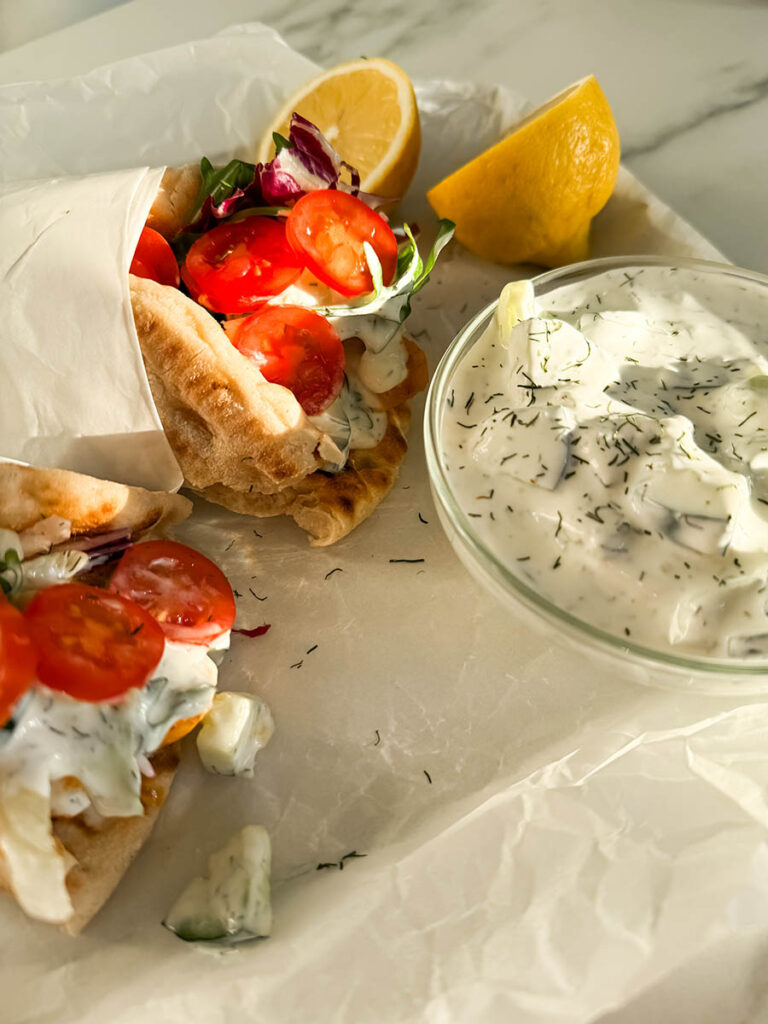 Simple Chicken Pitas, The Greek Way: Delicious And Quick 3 Golden-hour shot of chicken pitas, with soft pita bread cradling grilled chicken, crisp vegetables, and creamy tzatziki sauce. The warm lighting enhances the textures and colors, making the dish look fresh and inviting.