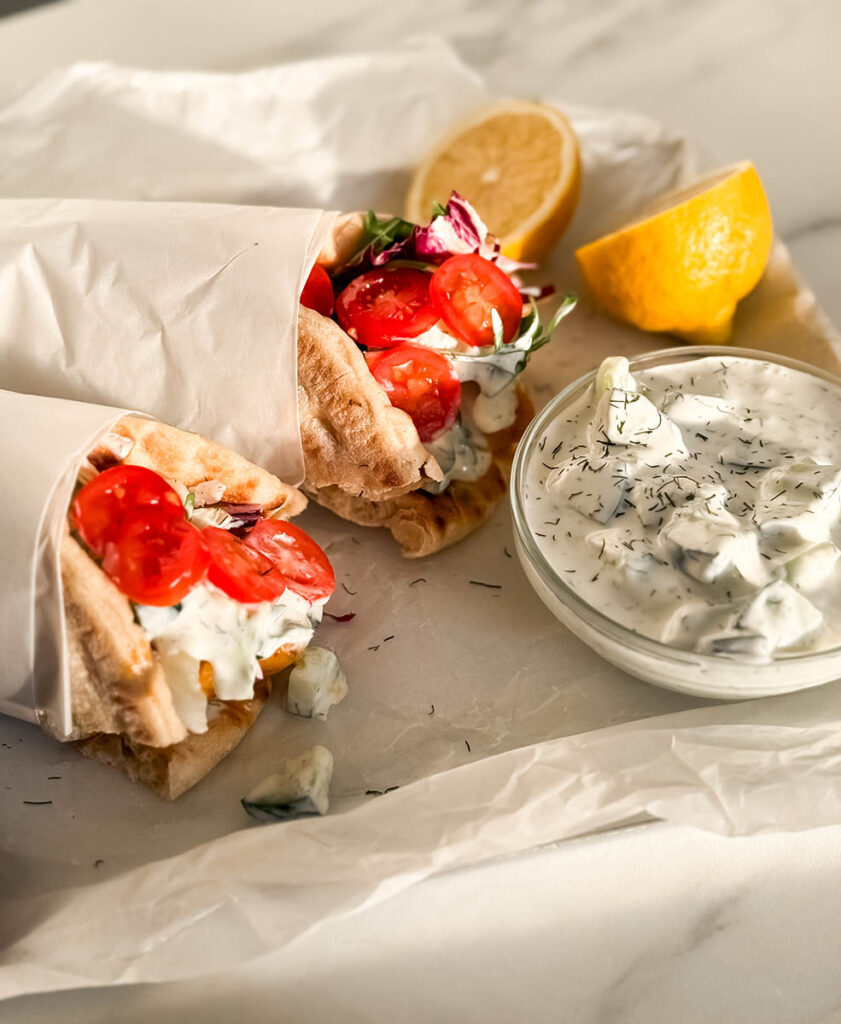 Simple Chicken Pitas, The Greek Way: Delicious And Quick 8 A cozy, rustic presentation of chicken pitas, with the soft, golden pita filled with seasoned chicken, crisp lettuce, juicy tomatoes, and a drizzle of tzatziki. Sunlight casts a warm glow over the meal, highlighting the fresh ingredients.