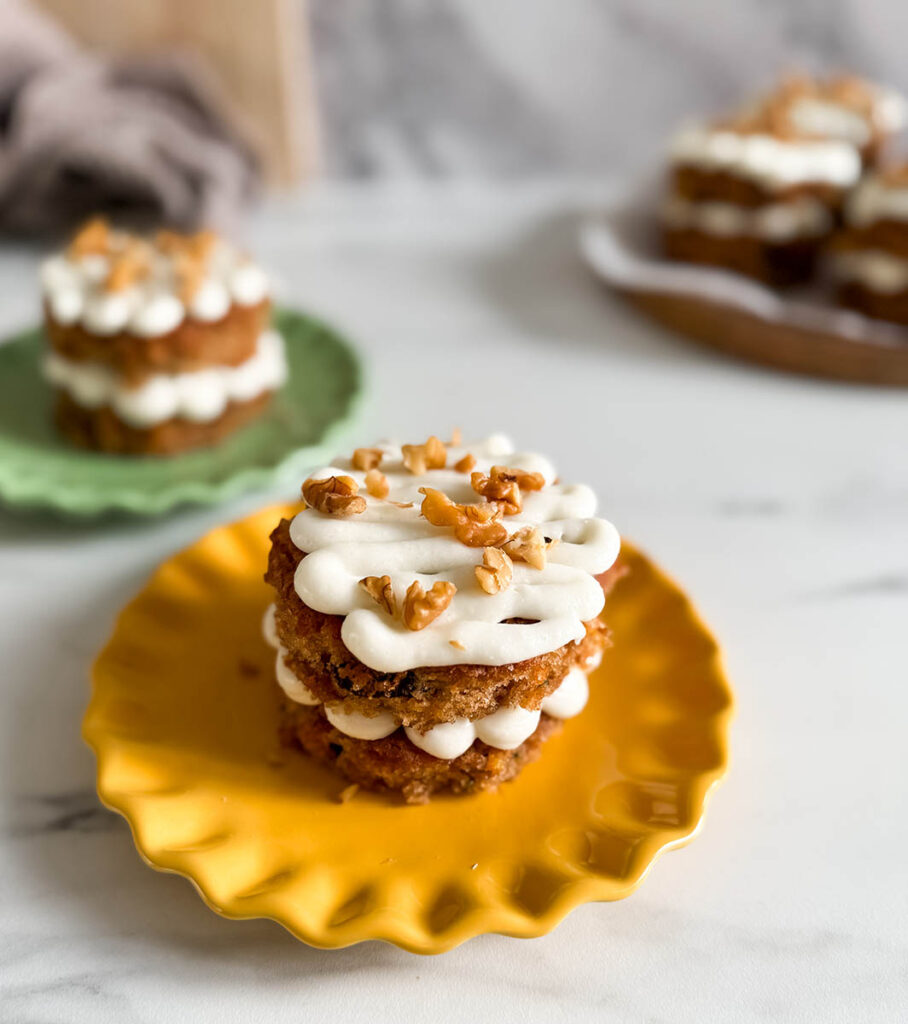 Side angle of a mini carrot cake, showing its moist texture with raisins and carrots, layered with frosting, and topped with chopped walnuts.