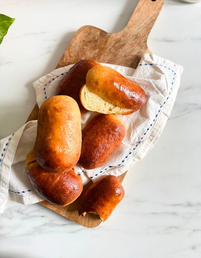 from top vegan hot dog buns on a towel on a wooden board, plant behind, on a marble background