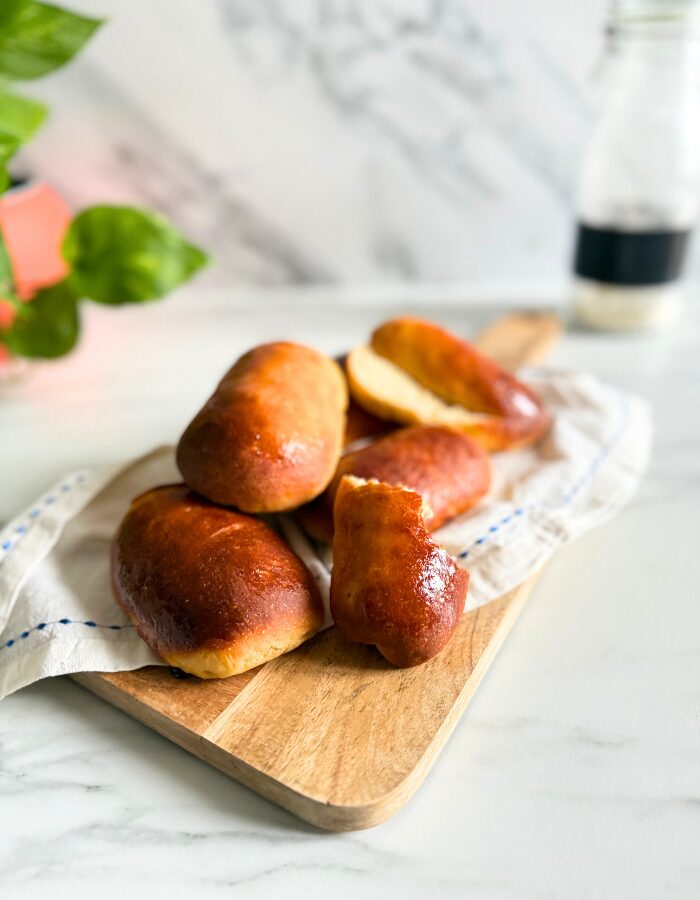 vegan hot dog buns on a towel on a wooden board, a bottle of flour and plant behind, on a marble background