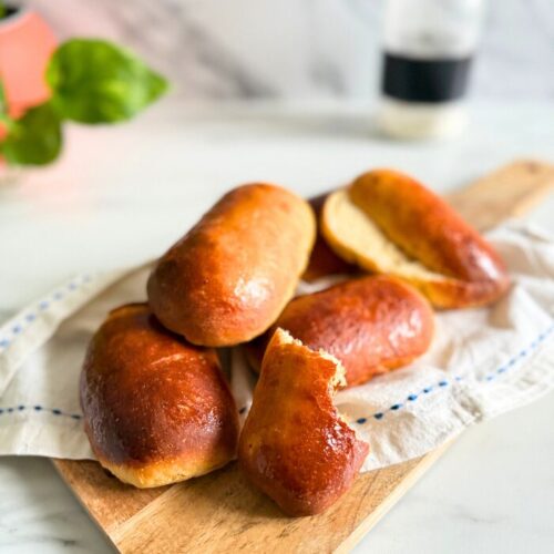 close up vegan hot dog buns on a towel on a wooden board, a bottle of flour and plant behind, on a marble background