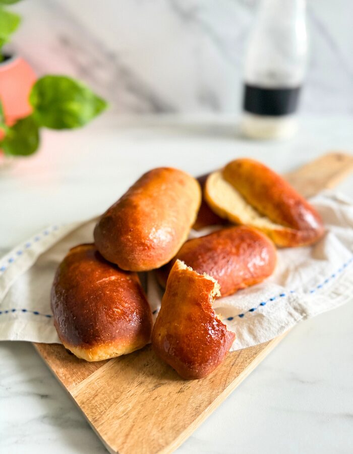 close up vegan hot dog buns on a towel on a wooden board, a bottle of flour and plant behind, on a marble background