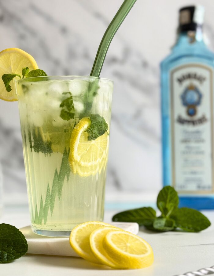 Easy Gin Mojitos - 5 Minute Twist On A Classic Mojito 9 close up of gin mojito in a glass with a straw and mint and lemon, on a marble coaster, behind wooden boards, a bottle of sapphire gin, marble background