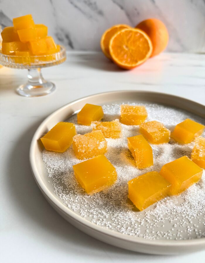 vegan fruit jellies on a cake stand, more fruit jellies on a plate in the back with sugar, oranges on a marble background