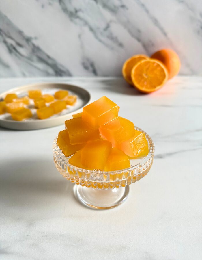 vegan fruit jellies on a cake stand, more fruit jellies on a plate in the back with sugar, oranges, on a marble background
