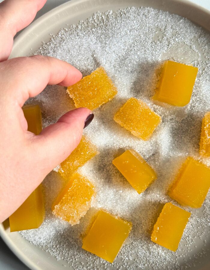 close up of vegan fruit jellies on a plate with sugar, fingers reaching for one