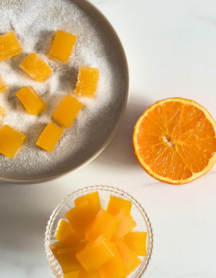 from top, vegan fruit jellies on a cake stand, more fruit jellies on a plate in the back with sugar, orange, on a marble background