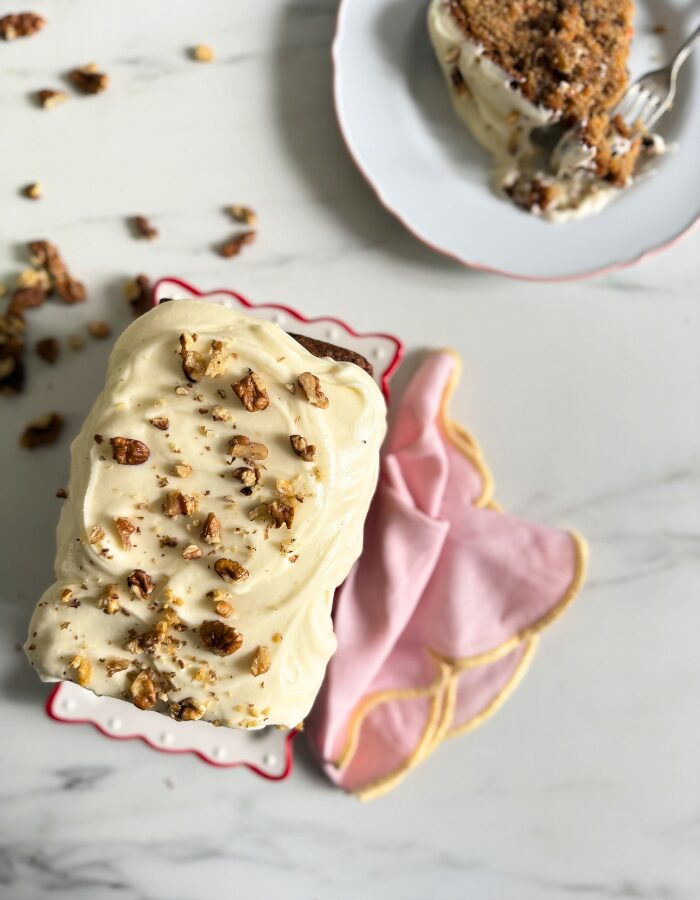 Delicious Carrot Cake Pound Cake With Cream Cheese Frosting 2 two plates with carrot cake pound cake, one with a slice and one with the rest of the cake, towel on the side, walnuts around, on marble background, from top