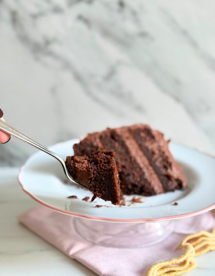slice of matildas cake, hand holding a fork with some of the cake, under a towel