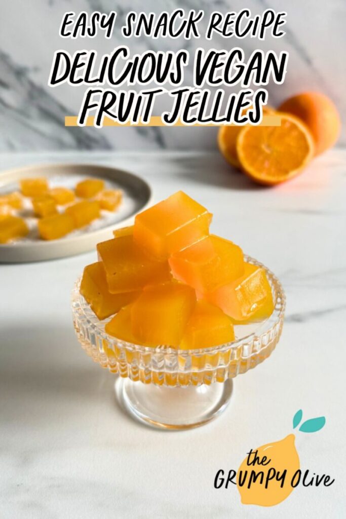 pin image vegan fruit jellies on a cake stand, more fruit jellies on a plate in the back with sugar, oranges and a glass of orange juice, on a marble background