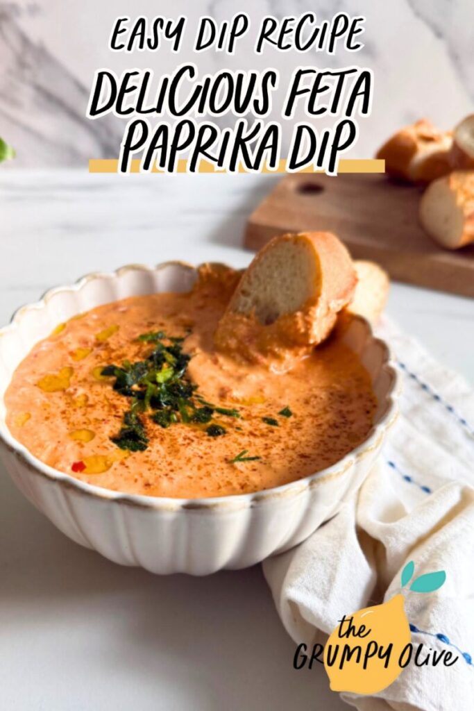 pin image paprika dip in a bowl with a slice of bread, more bread on a wooden board behind and some on the side, a towel, a plant, on a marble background